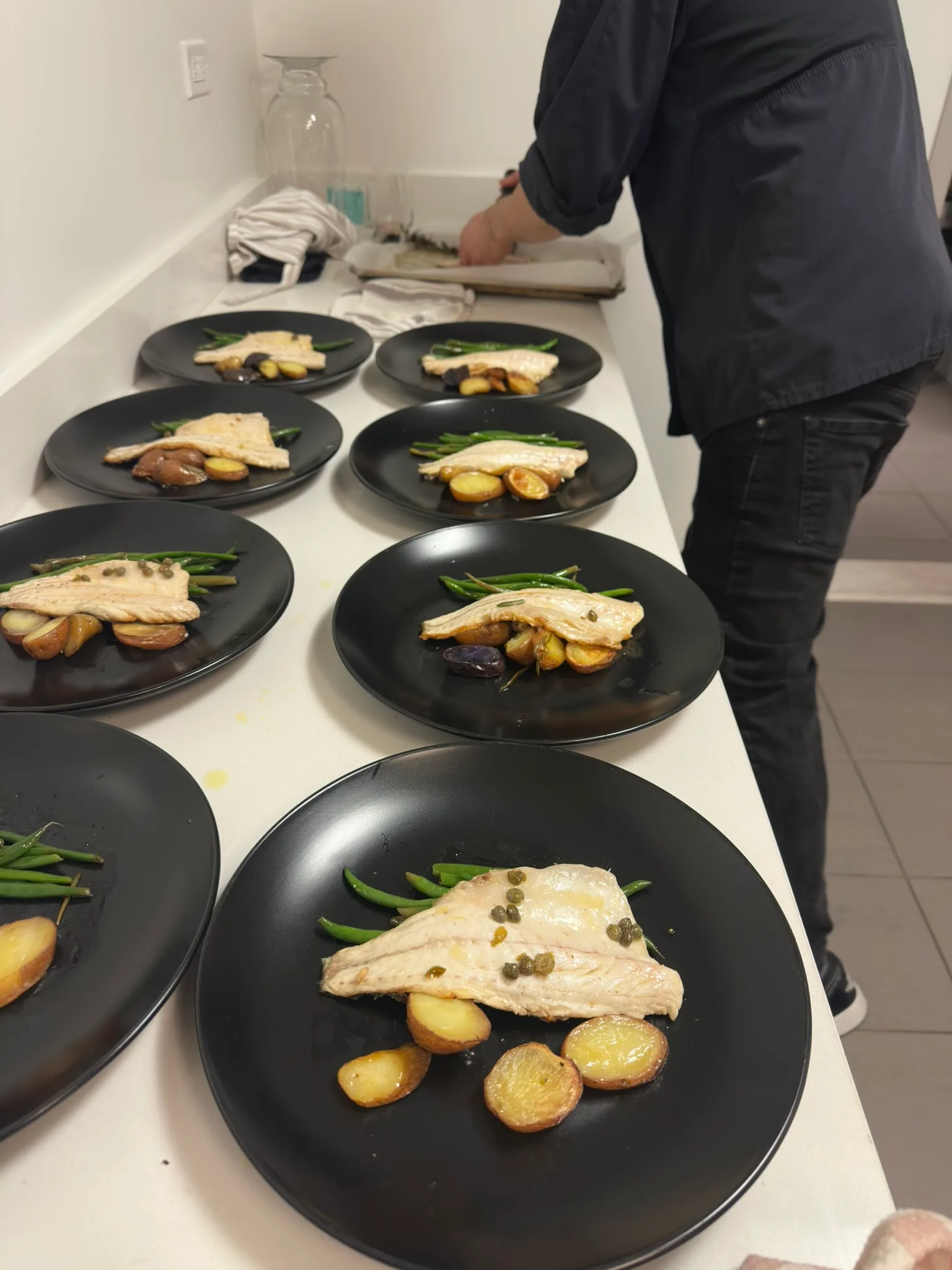 Pan-seared fish with green beans, capers, and roasted potatoes on black plates