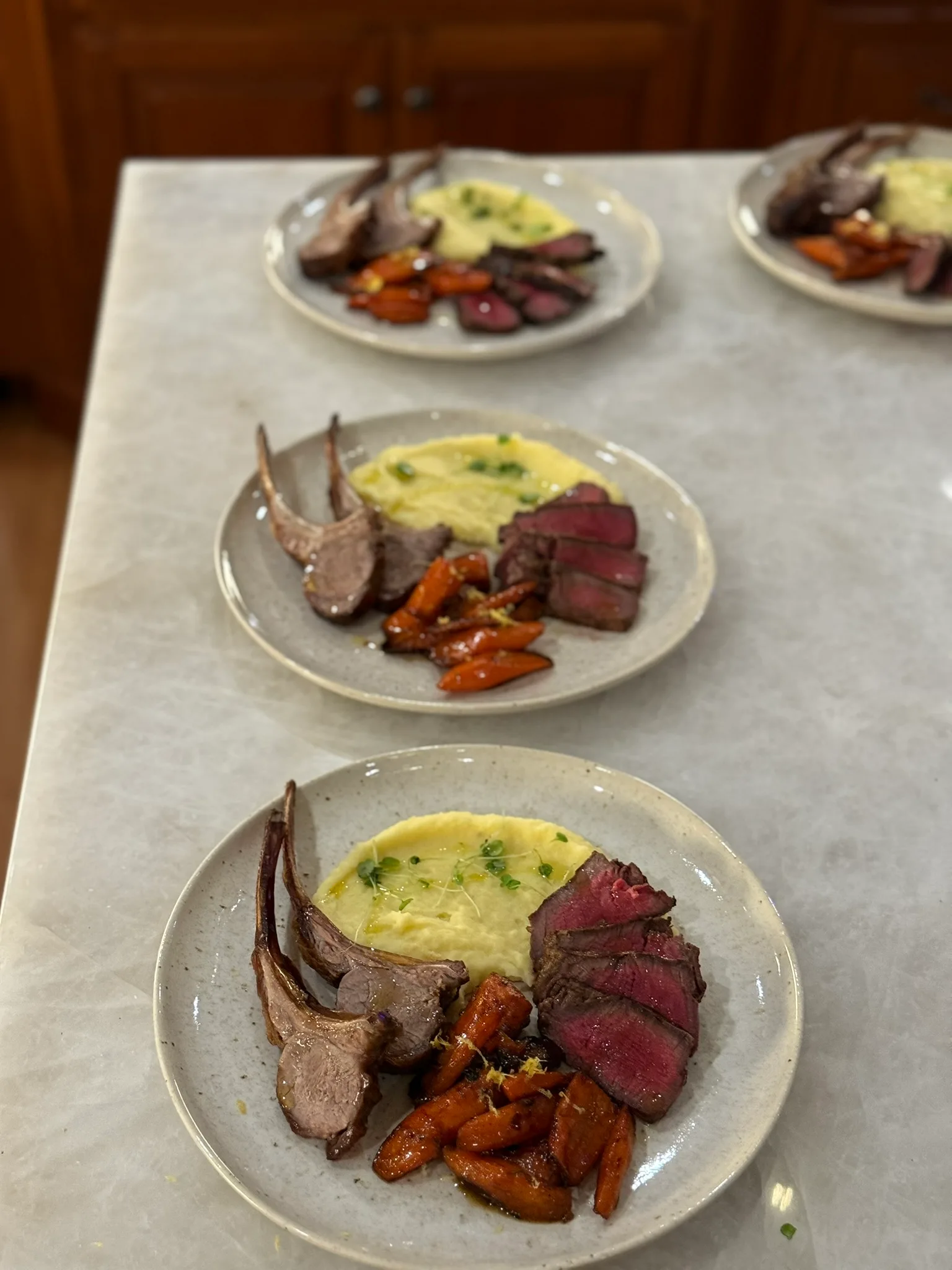Multiple plates of lamb chops with creamy polenta and roasted carrots