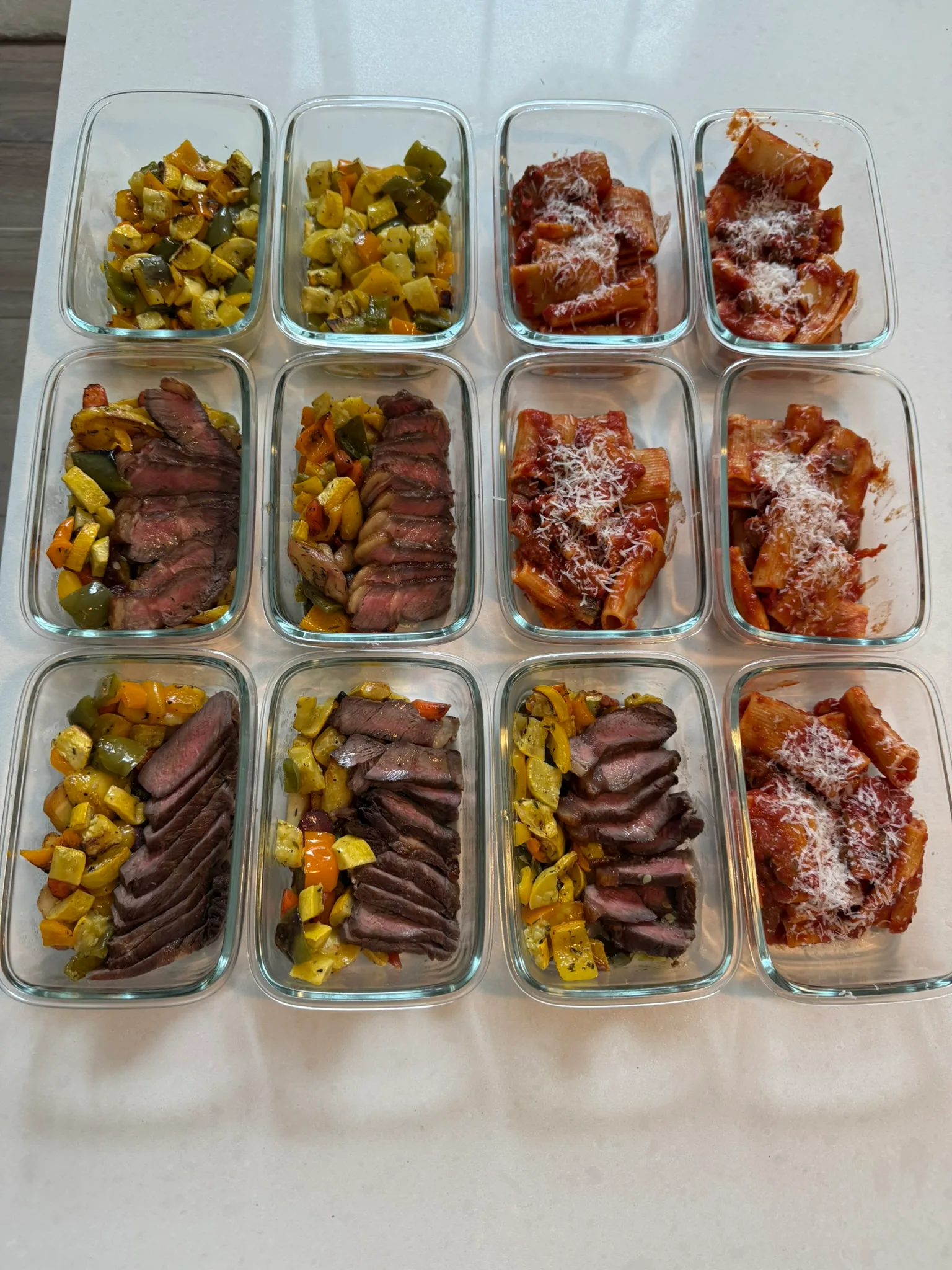 Meal prep grid with sliced steak, roasted veggies, and rigatoni in glass containers